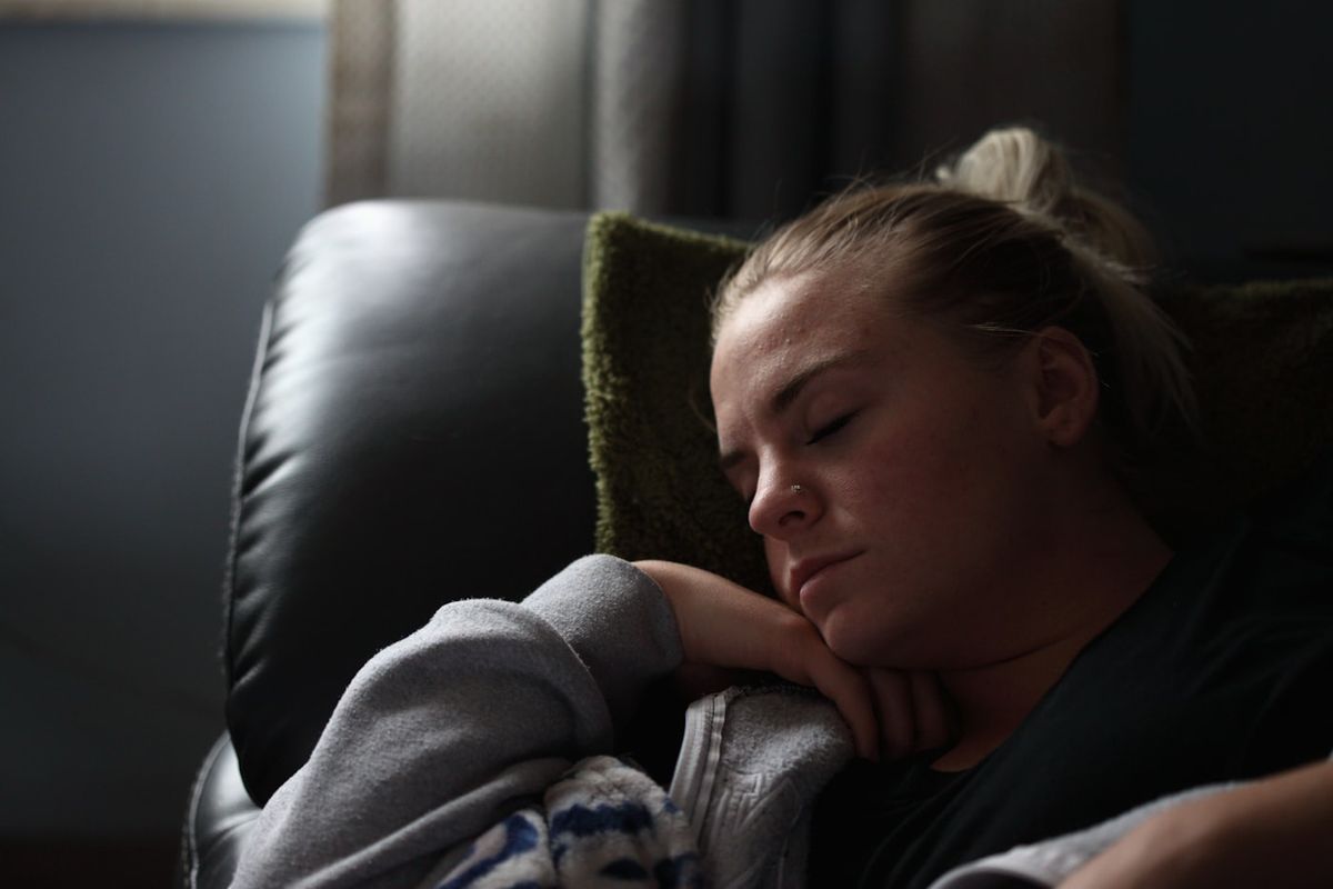 Ung person i genser som hviler utmattet på en sofa