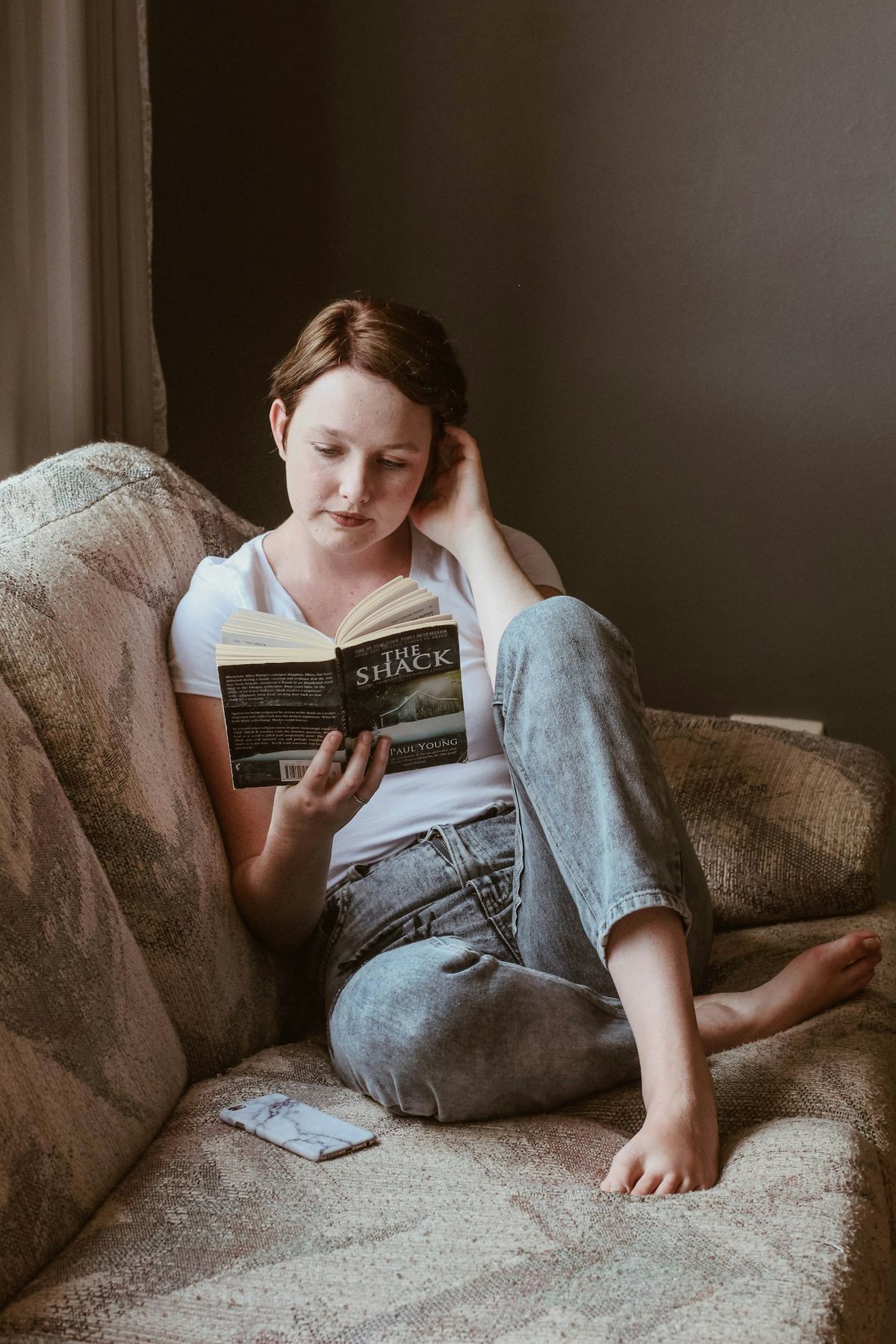 Ung kvinne som hviler og leser i sofaen under rekonvalesens